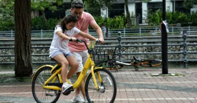 Father teaches daughter to ride a yellow bicycle in a Singapore park. Bonding moment.