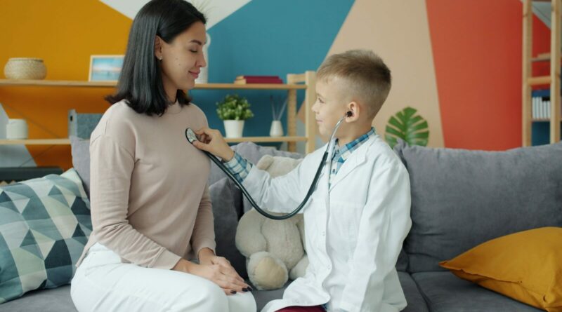 Boy in doctor's coat listens to mother's chest